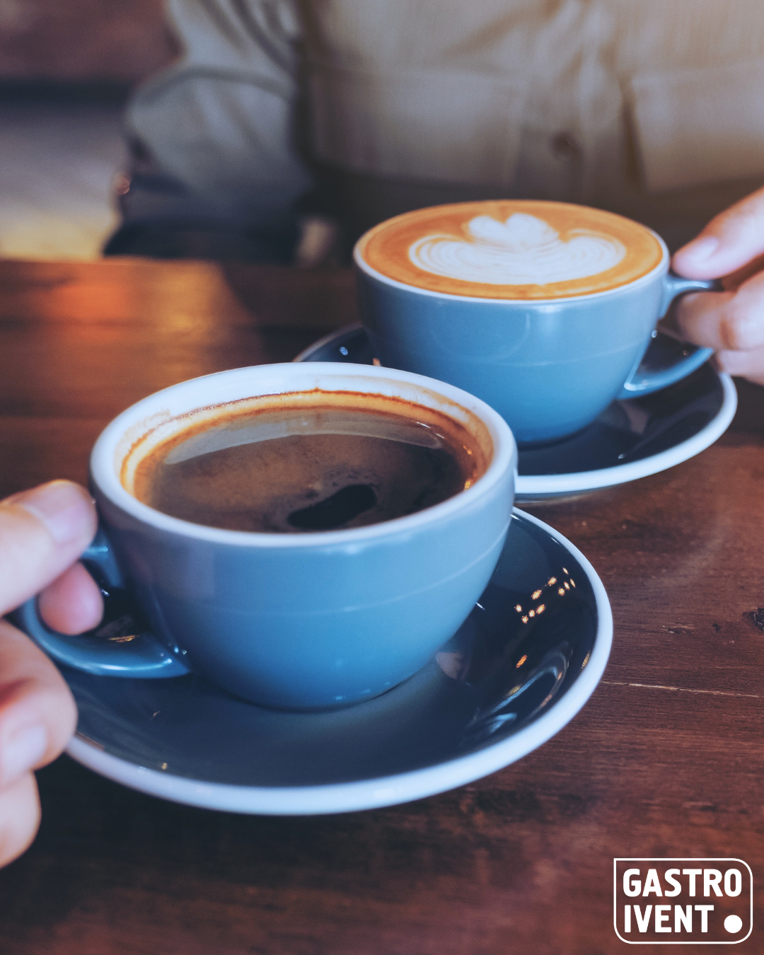 Zwei blaue Tassen, die auf einer Untertasse stehen und mit Kaffee befüllt sind.
