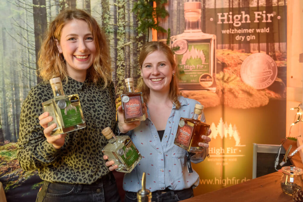 Zwei Austellerinnen zeigen ihre Gin-Flaschen und lächeln den Betrachter an