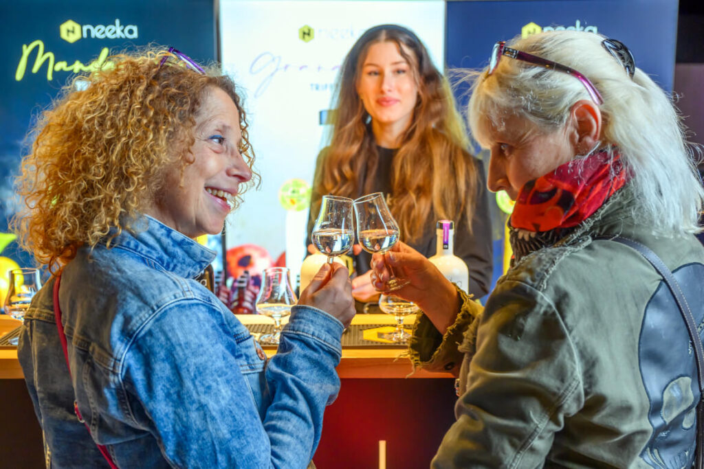 Zwei Besucherinnen stoßen am Ausstellerstand mit Tasting-Gläsern an