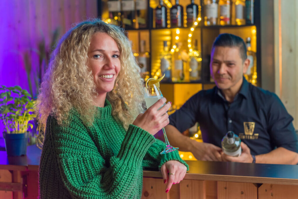 Frau mit einem Glas Gin an der Ginothek, ein Barkeeper im Hintergrund