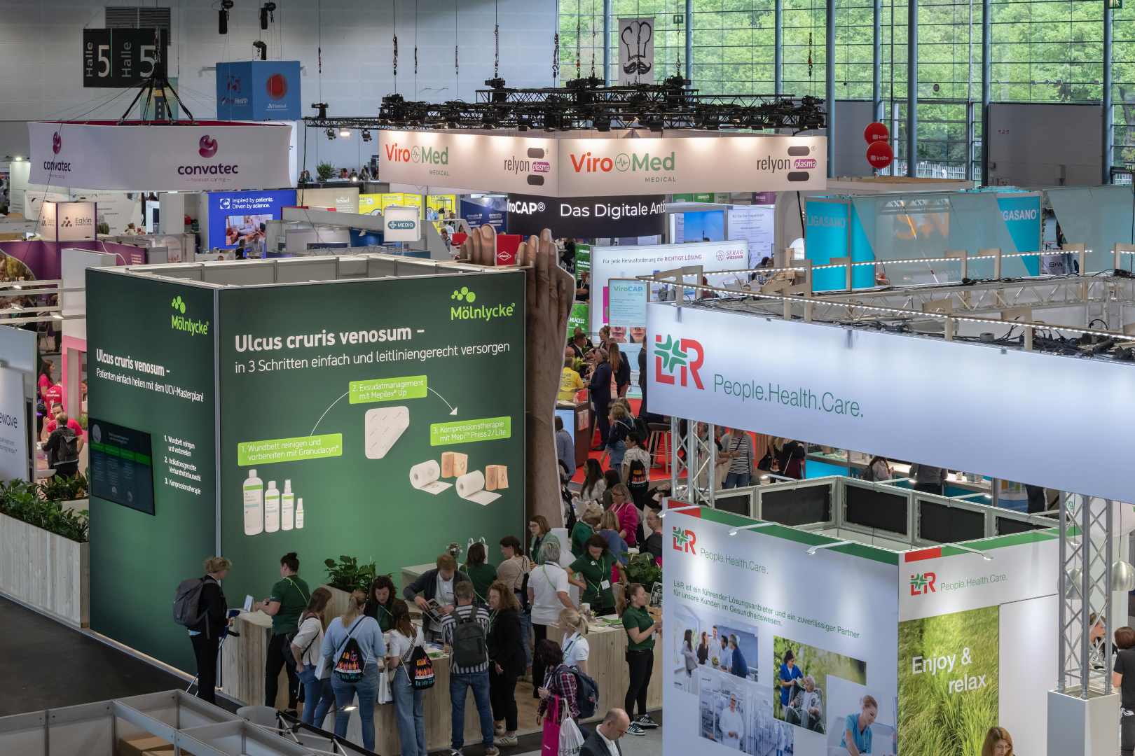 Blick auf die gut besuchte Fachausstellung des DEWU Deutschen Wundkongresses mit zahlreichen Messeständen. Besuchende informieren sich und führen Gespräche an den Ständen.